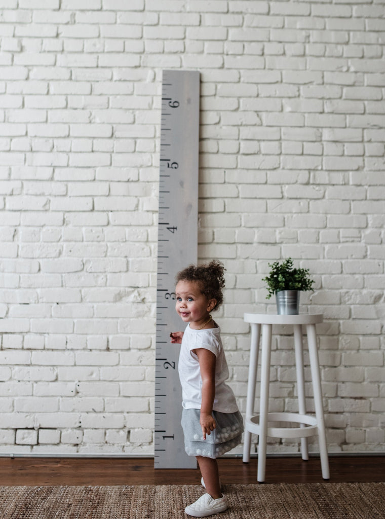 little-girl-standing-next-to-nursery-decor-gray-wood-with-white-painted-brick-walls